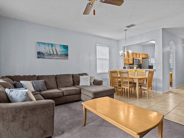 carpeted living room featuring a textured ceiling and ceiling fan with notable chandelier