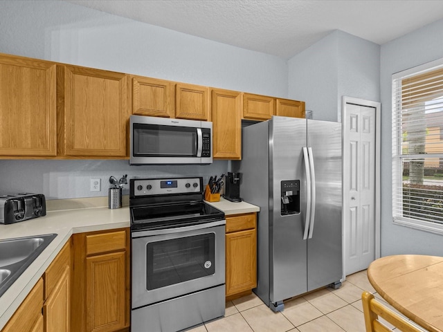 kitchen featuring a wealth of natural light, light tile patterned floors, a textured ceiling, and appliances with stainless steel finishes