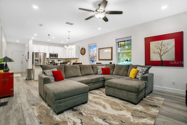 living room with ceiling fan with notable chandelier and light wood-type flooring