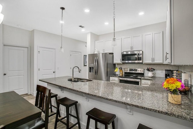 kitchen featuring kitchen peninsula, appliances with stainless steel finishes, sink, pendant lighting, and white cabinets