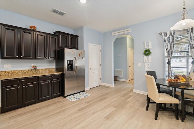 kitchen with dark brown cabinetry, stainless steel fridge with ice dispenser, light stone counters, pendant lighting, and light hardwood / wood-style floors