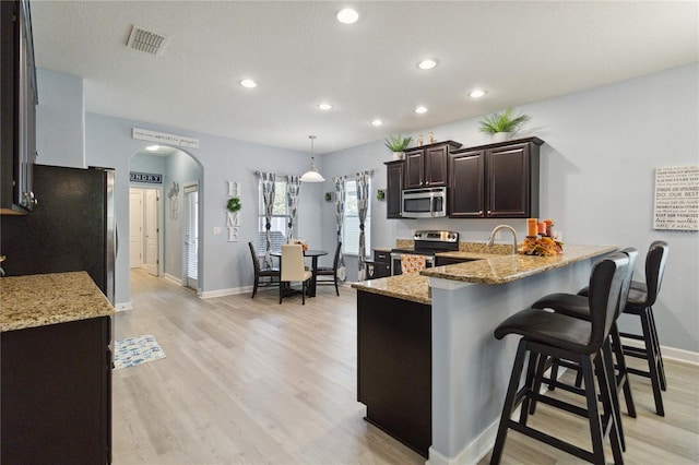 kitchen featuring pendant lighting, light hardwood / wood-style flooring, light stone countertops, appliances with stainless steel finishes, and a breakfast bar area