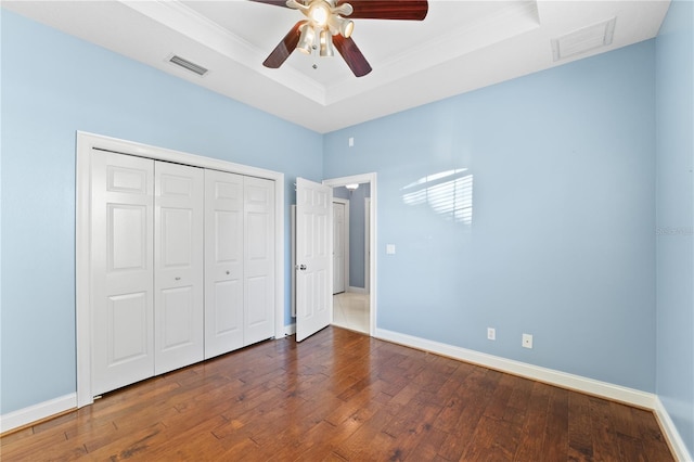 unfurnished bedroom with ceiling fan, dark hardwood / wood-style floors, ornamental molding, a tray ceiling, and a closet