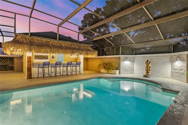 pool at dusk with a patio area, a lanai, and a bar