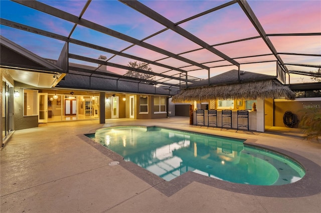 pool at dusk with a patio, glass enclosure, and an outdoor bar