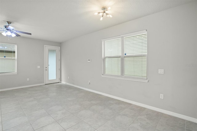 spare room with a textured ceiling, light tile patterned flooring, a healthy amount of sunlight, and ceiling fan with notable chandelier