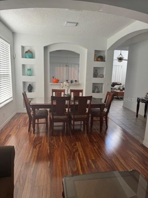 dining room with built in shelves, ceiling fan, dark hardwood / wood-style flooring, and a textured ceiling