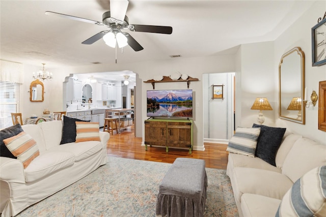 living room with ceiling fan with notable chandelier and light hardwood / wood-style flooring