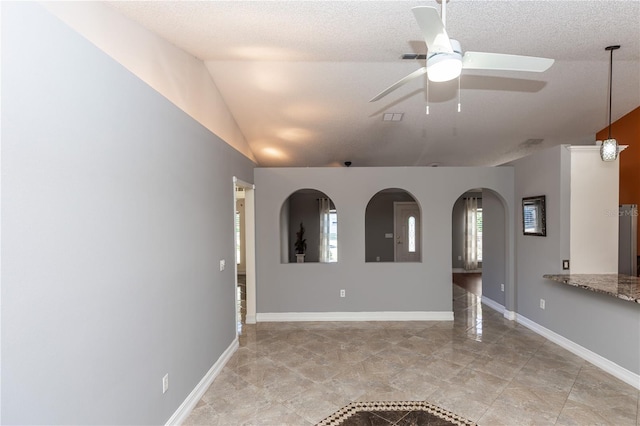 unfurnished room with arched walkways, vaulted ceiling, a textured ceiling, and baseboards