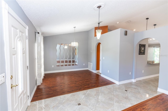 unfurnished room featuring visible vents, arched walkways, lofted ceiling, light wood-style flooring, and a textured ceiling