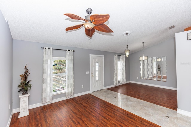 entryway featuring visible vents, vaulted ceiling, a textured ceiling, wood finished floors, and baseboards