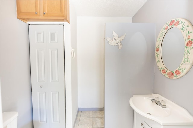 bathroom with a textured ceiling, tile patterned flooring, toilet, a sink, and a closet