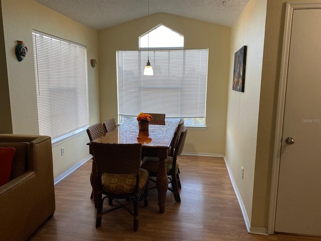 dining area with a textured ceiling, wood-type flooring, and vaulted ceiling