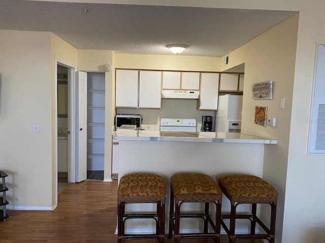 kitchen featuring dark wood-type flooring, a kitchen breakfast bar, kitchen peninsula, white appliances, and white cabinets