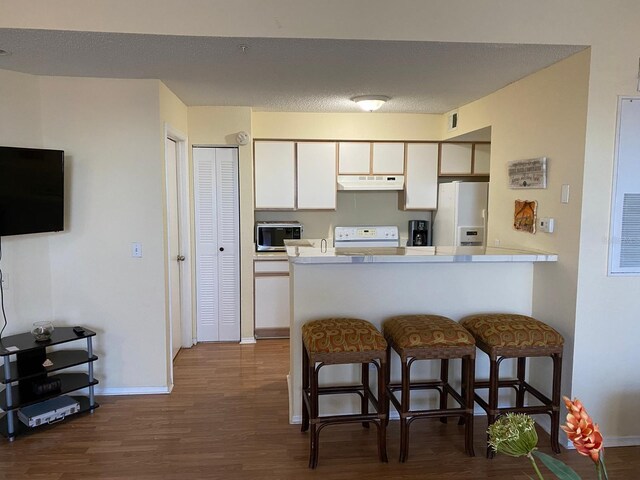 kitchen featuring white cabinetry, a kitchen breakfast bar, dark hardwood / wood-style flooring, kitchen peninsula, and white appliances