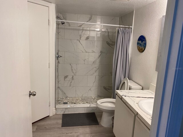 bathroom with a shower with curtain, hardwood / wood-style floors, a textured ceiling, toilet, and vanity