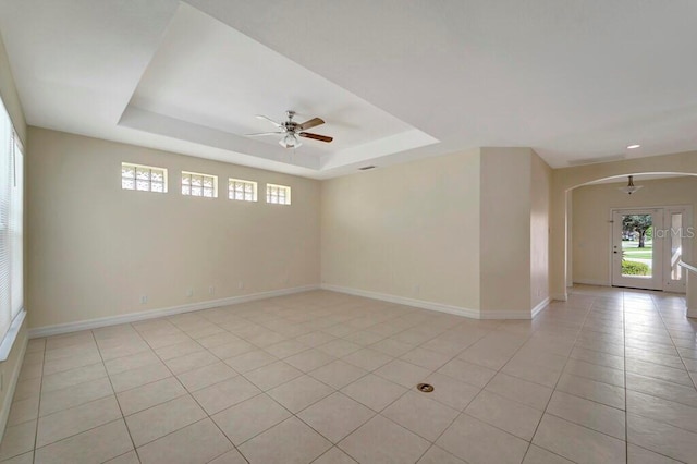 tiled empty room with a raised ceiling and ceiling fan