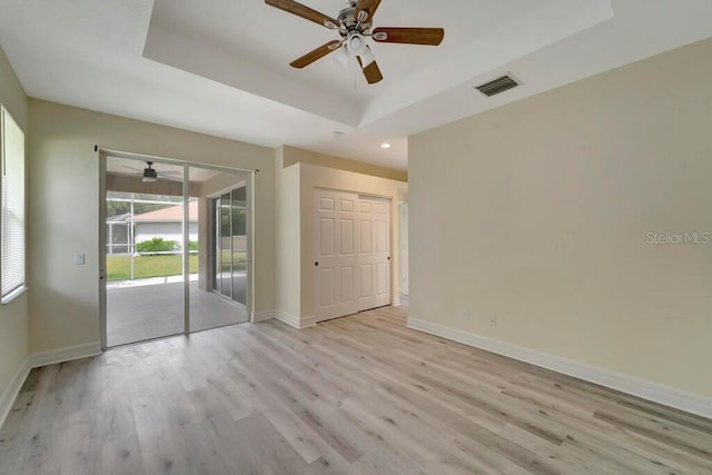 empty room with a raised ceiling, ceiling fan, and light hardwood / wood-style flooring