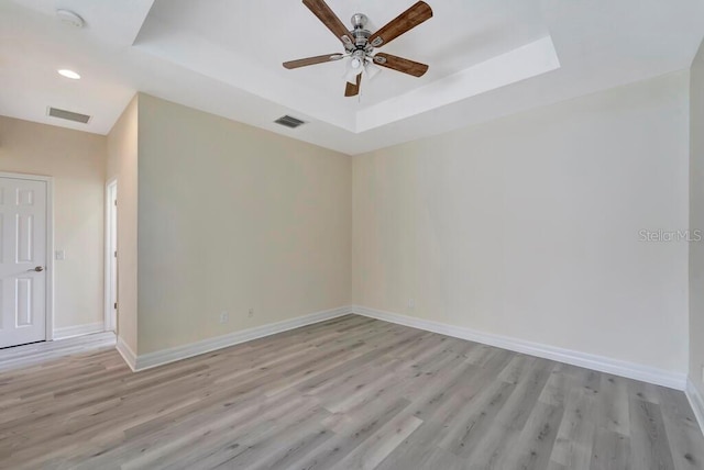 empty room featuring a tray ceiling, light hardwood / wood-style flooring, and ceiling fan