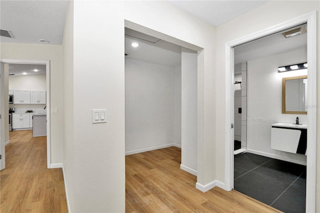 corridor featuring a textured ceiling, light hardwood / wood-style floors, and sink