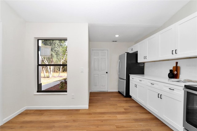 kitchen with white cabinets, appliances with stainless steel finishes, backsplash, and light hardwood / wood-style floors