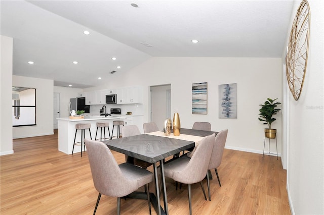 dining area with light hardwood / wood-style floors, vaulted ceiling, and sink