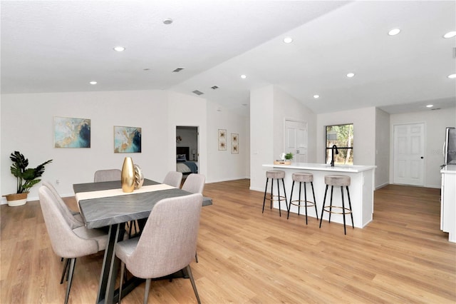 dining room with vaulted ceiling, sink, and light hardwood / wood-style flooring