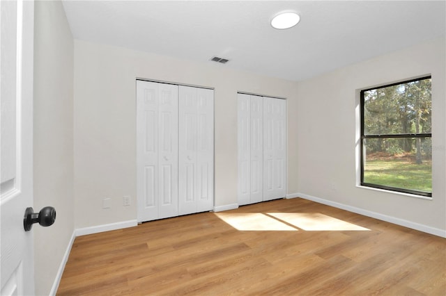 unfurnished bedroom with two closets and light wood-type flooring