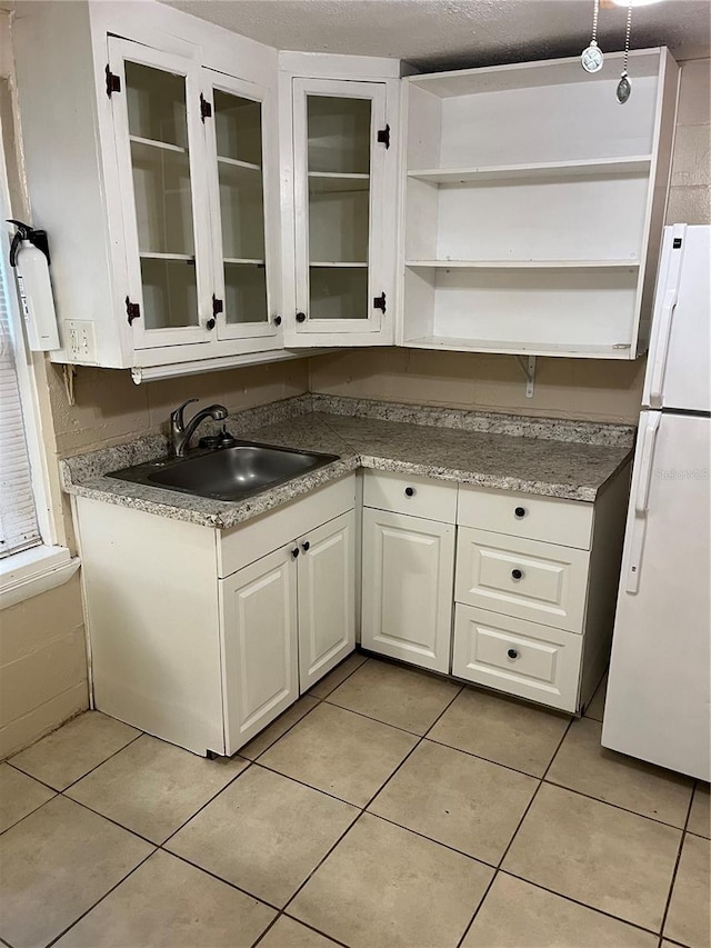 kitchen featuring sink, light tile patterned flooring, white fridge, a textured ceiling, and white cabinets