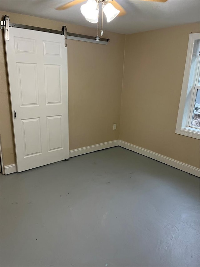 unfurnished room featuring a barn door, concrete floors, and ceiling fan