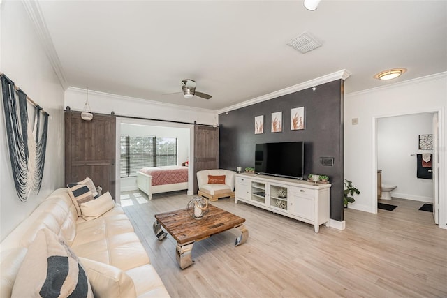 living room with ceiling fan, light hardwood / wood-style flooring, ornamental molding, and a barn door