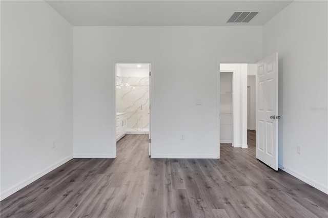 unfurnished bedroom with a closet, light wood-type flooring, a spacious closet, and ensuite bath