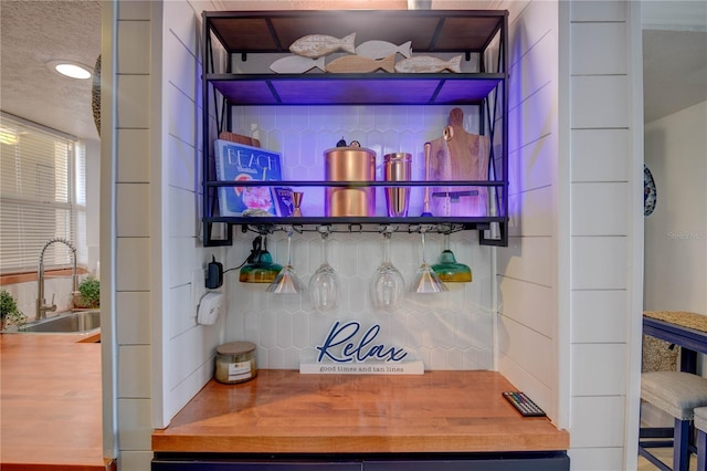 bar with a textured ceiling, tasteful backsplash, butcher block countertops, and sink