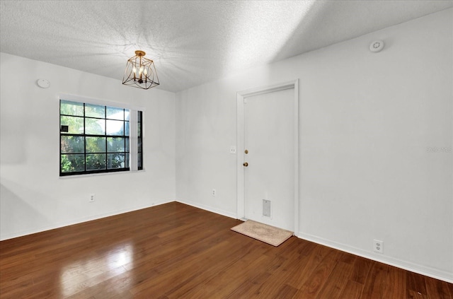 empty room featuring hardwood / wood-style floors, a textured ceiling, and a notable chandelier