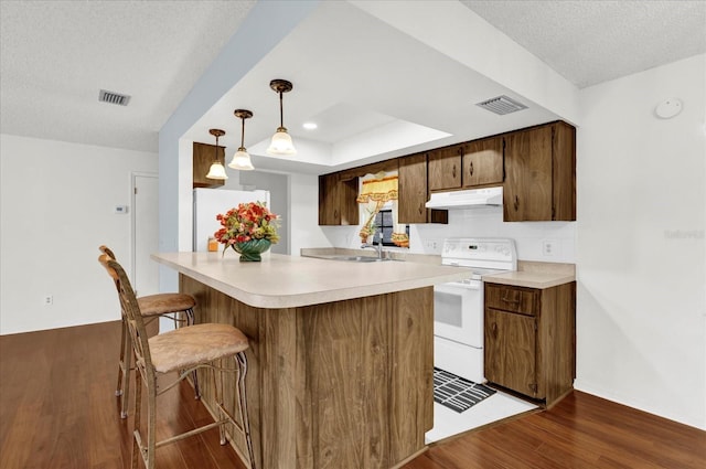 kitchen featuring kitchen peninsula, a textured ceiling, white appliances, decorative light fixtures, and dark hardwood / wood-style floors