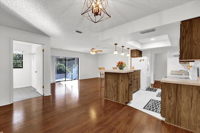 kitchen featuring kitchen peninsula, light wood-type flooring, ceiling fan with notable chandelier, sink, and white refrigerator with ice dispenser