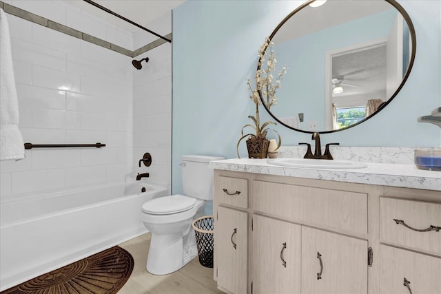 full bathroom with vanity, tiled shower / bath, hardwood / wood-style flooring, ceiling fan, and toilet