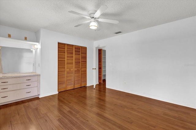 unfurnished bedroom with a textured ceiling, a closet, ceiling fan, and dark wood-type flooring