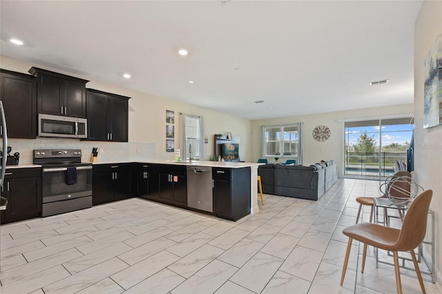 kitchen with sink, kitchen peninsula, decorative backsplash, a breakfast bar, and appliances with stainless steel finishes