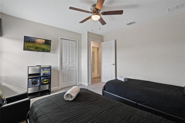 bedroom with a textured ceiling, ceiling fan, light carpet, and a closet