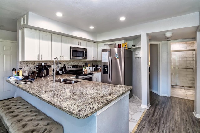 kitchen featuring sink, light hardwood / wood-style flooring, kitchen peninsula, white cabinets, and appliances with stainless steel finishes