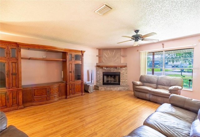 living room featuring ceiling fan, a fireplace, a textured ceiling, and light wood-type flooring