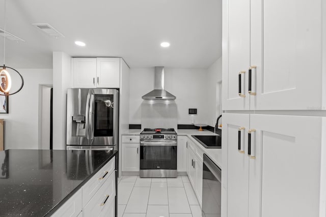 kitchen with sink, wall chimney range hood, dark stone countertops, white cabinets, and appliances with stainless steel finishes