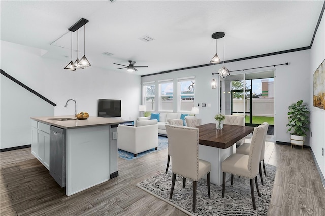 dining area featuring wood-type flooring, ceiling fan, ornamental molding, and sink