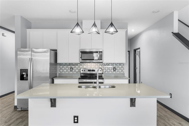 kitchen with appliances with stainless steel finishes, a kitchen island with sink, sink, white cabinets, and hanging light fixtures