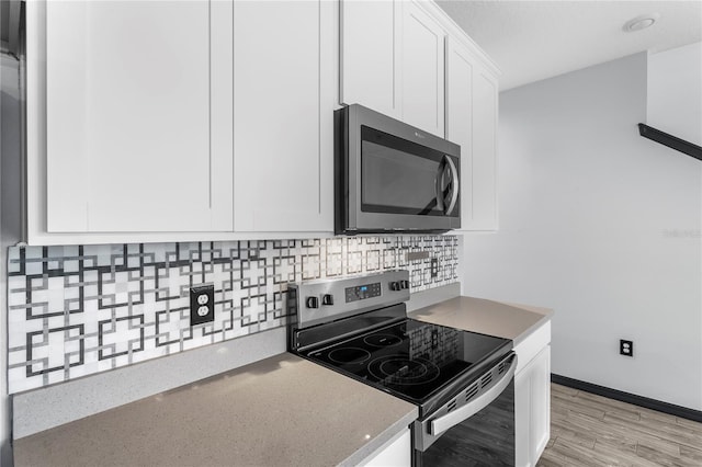 kitchen with tasteful backsplash, white cabinets, light hardwood / wood-style floors, and appliances with stainless steel finishes