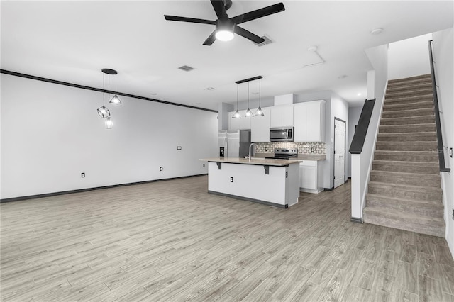 kitchen with appliances with stainless steel finishes, an island with sink, decorative light fixtures, white cabinets, and light wood-type flooring