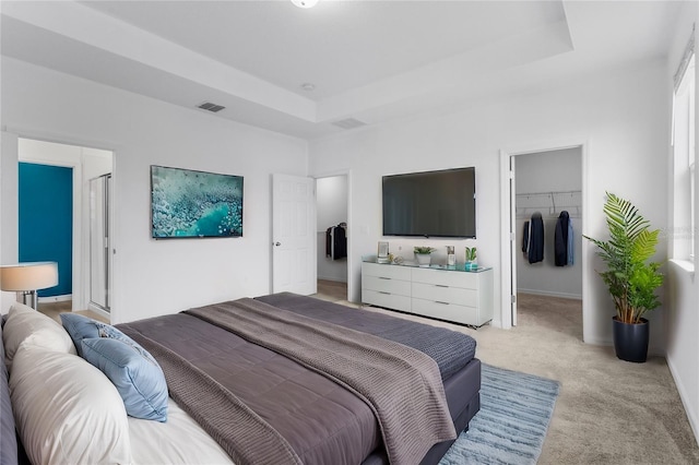 bedroom with a raised ceiling, light colored carpet, a walk in closet, and a closet