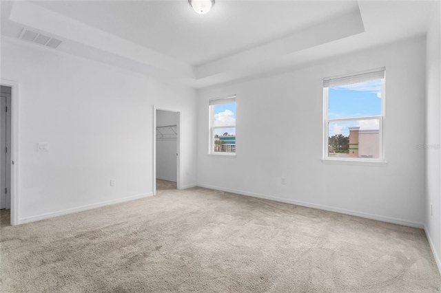 unfurnished bedroom with carpet flooring, a raised ceiling, a spacious closet, and a closet