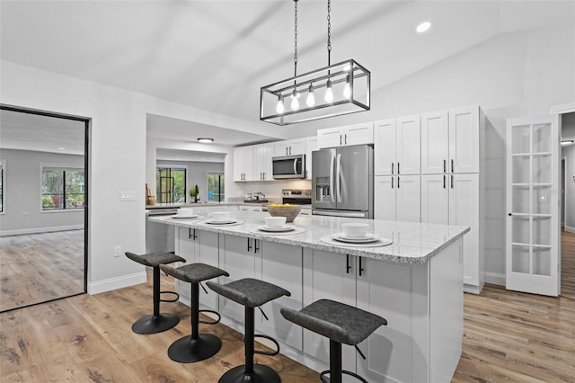 kitchen with white cabinets, light stone countertops, appliances with stainless steel finishes, and vaulted ceiling